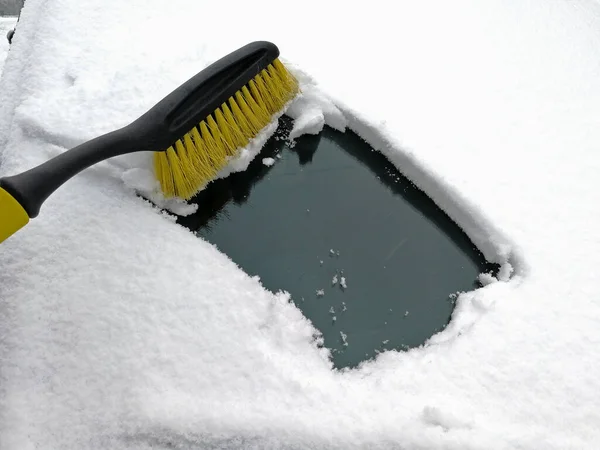 the driver cleans the windscreen of the car with a brush from the thick cover of snow. Maintenance and care of the car in winter