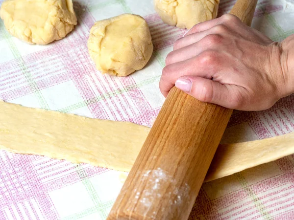 the Baker rolls the dough into strips on the kitchen table, sprinkled with flour.