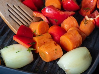 Taze sebzeler, ahşap bir spatulayla karıştırılmış ızgarada pişirilir. Havuç, tatlı kırmızı biber, soğan. Vejetaryen ve sağlıklı yemek kavramı..