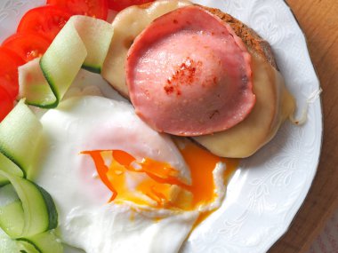 Ready-made Breakfast of eggs with liquid yolk, sausage and cheese sandwich decorated with tomatoes and cucumber slices