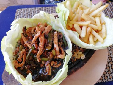 Tavuk Sizzler lahana yapraklarıyla servis ediliyor. Cızırdayan bir tavada pişirilmiş bir yemek.