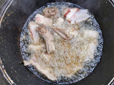 Dilimlenmiş et parçaları, kemiğin üzerinde kaynayan yağda bir kazanda pişirilir..