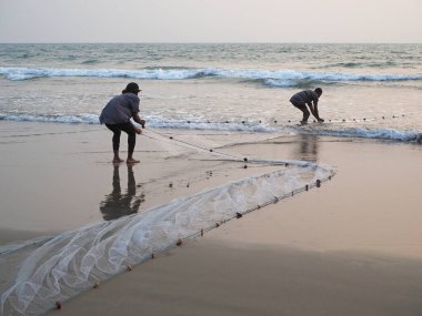 Morjim, GOA, INDIA, 28.02.2020 Balıkçılar gün batımında denizden bir balık ağı çıkarıyorlar.