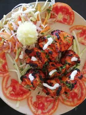 Hint tavuğu Tikka tandır, domates halkalarının üzerine serilmiş ve salatayla süslenmiş.