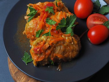 Et, pirinç ve sebzeli lahana ruloları. Doldurulmuş Pekin lahana yaprakları et, domates sosu, domates ve otlarla dolu siyah bir tabakta..