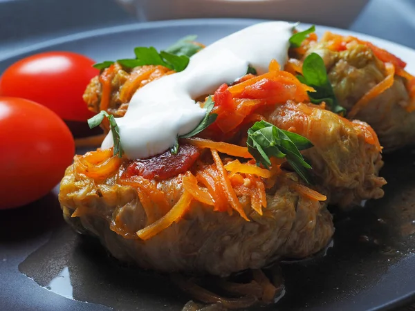 Et, pirinç ve sebzeli lahana ruloları. Doldurulmuş Pekin lahana yaprakları domates soslu, domates ve otlarla dolu siyah bir tabakta. Stüdyo çekimi, kapat.