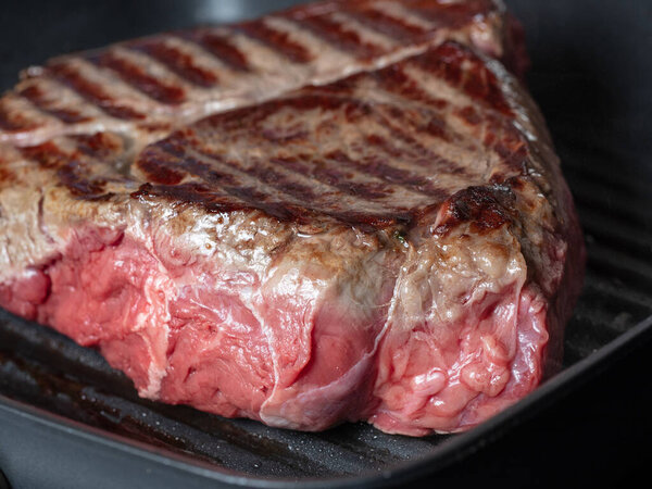 A large piece of juicy fresh beef fried on one side in a pan-grill. Stripes-rare, the juice from the meat. Close up, front view