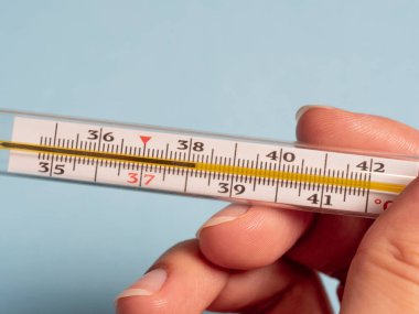 Mavi arka planda izole edilmiş bir kadının elindeki cıva termometre. Termometre kullanarak sıcaklık ölçümü. Yüksek ateş ve hastalık