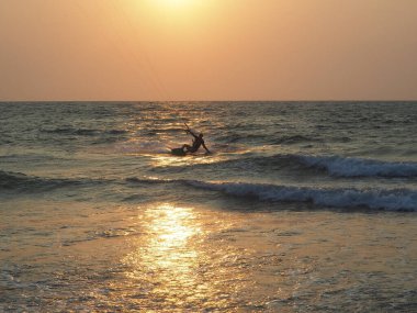 Batan güneşin ışınlarında uçurtmalarla denizde at süren bir adamın silueti. Aşırı su sporları