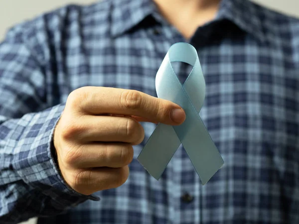 A man in a checked shirt holds a blue ribbon in his hand-a symbol of prostate cancer awareness.Concept of medicine and human health