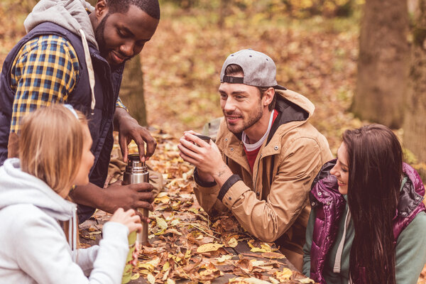 Friends pouring hot drink in forest