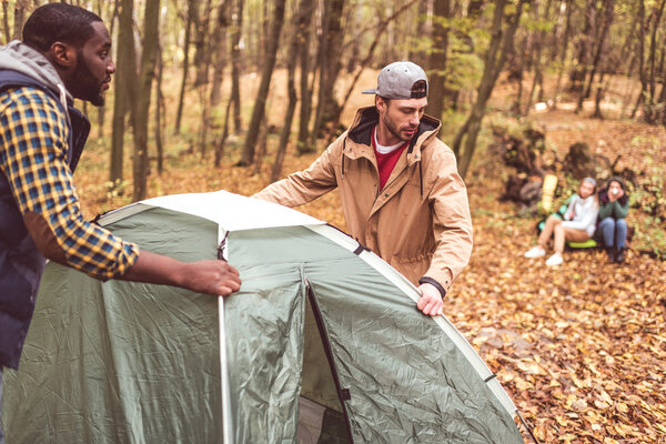Men pitching tent in autumn forest 
