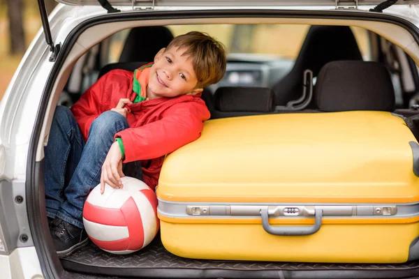Smiling boy sitting in car trunk — Stockfoto