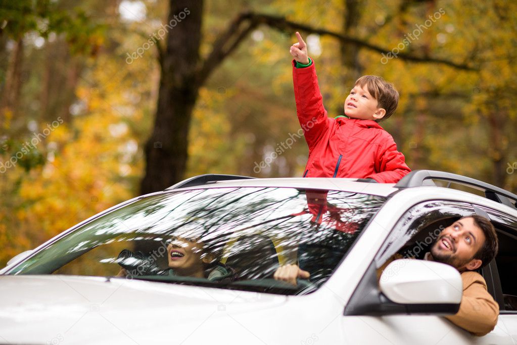 Adorable boy standing in car sunroof 