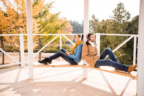 Young couple sitting on bench in headphones — Stock Photo, Image