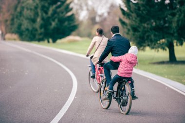 Family riding bicycles in park clipart