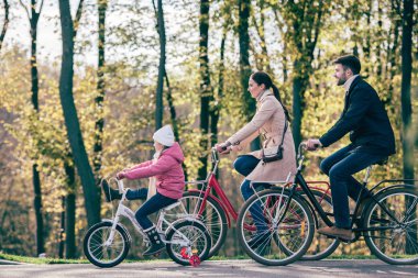 Happy family riding bikes in park clipart