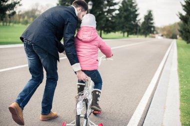 Babası kızına bisiklet sürmeyi öğretiyor.