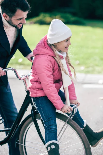 Отец несет улыбающуюся дочь на велосипеде — стоковое фото