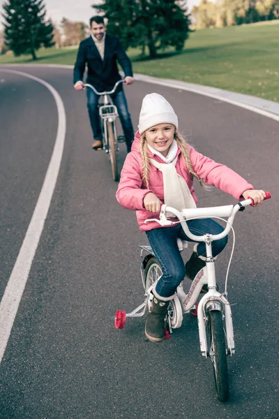 Sorrindo menina de bicicleta com o pai — Fotografia de Stock