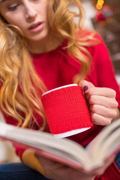 Жінка читає книгу з гарячим напоєм — стокове фото