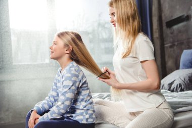 Mother combing hair of daughter clipart