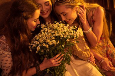 women in boho style smelling flowers