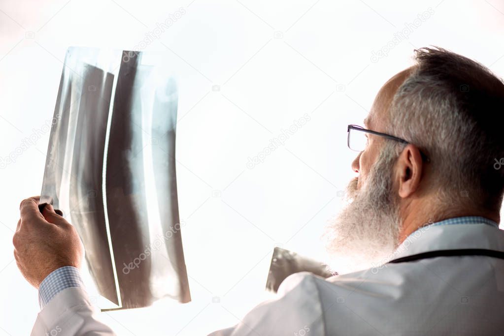 Senior bearded male doctor in eyeglasses holding x-ray image on white