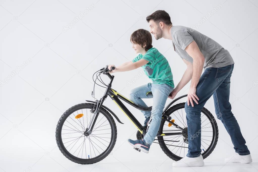 father helping son to ride bicycle