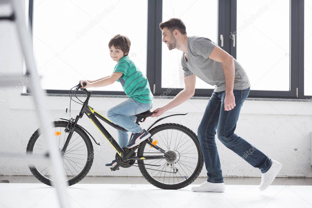father helping son to ride bicycle