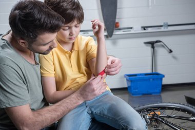 Father putting patch on son  clipart