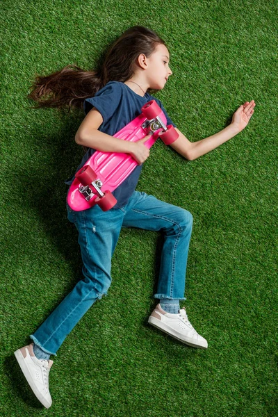 Menina com skate deitado na grama — Fotos gratuitas