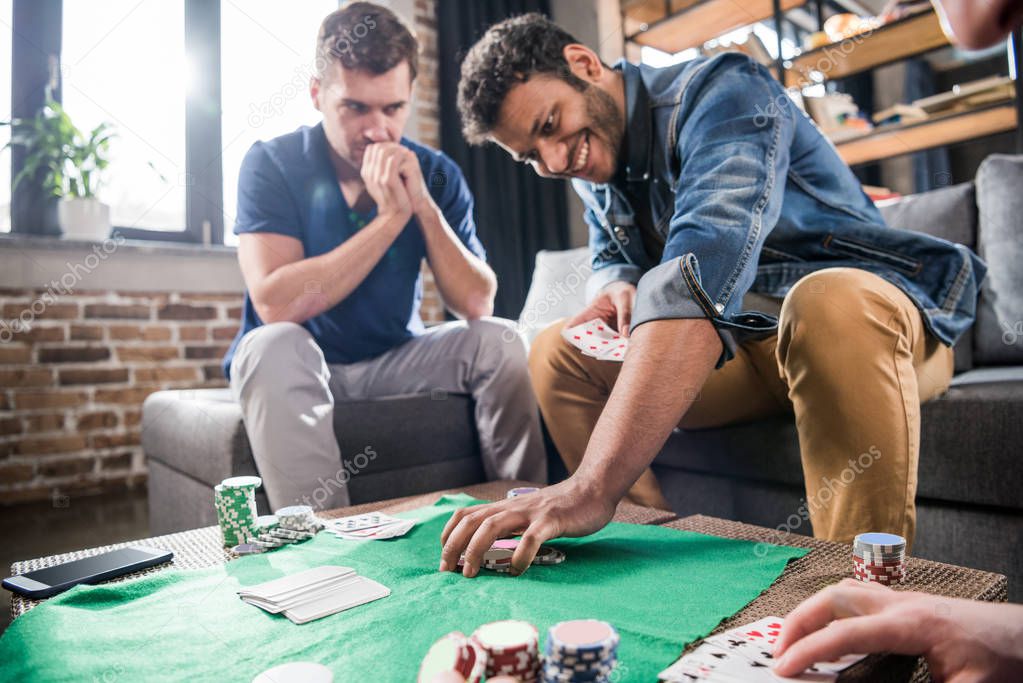 Young men playing cards at gaming table, young people having fun concept