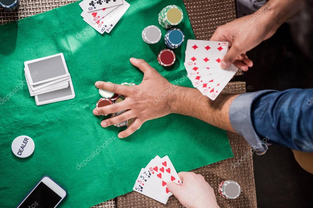 Close-up partial view of men with cards and chips at betting table