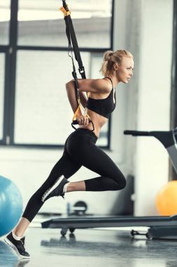 Blonde fitness woman training with trx fitness straps clipart
