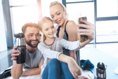 Girl taking self portrait with parents at fitness center