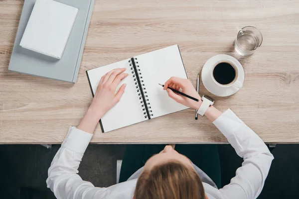 Frau sitzt am Tisch und macht sich Notizen — Stockfoto