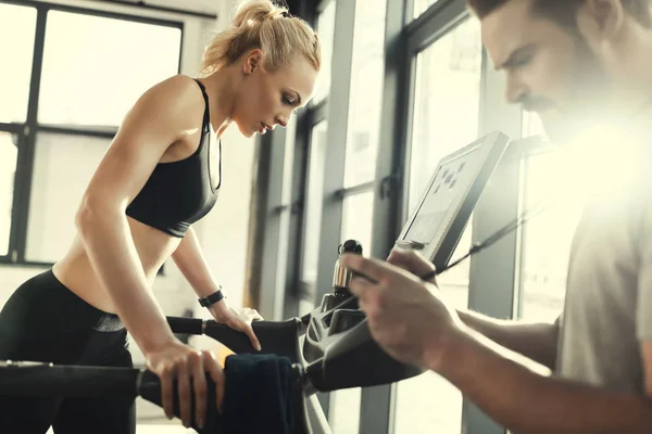Kobieta blonde treningu na bieżni i trener z zegarem, widok z boku — Zdjęcie stockowe