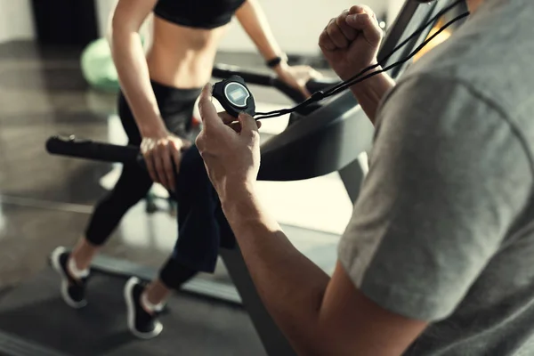 Kvinna träning på löpband och tränare med timer, sidovy — Stockfoto