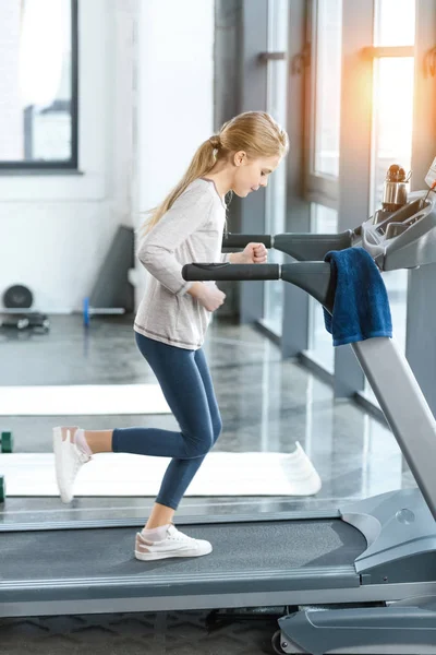Blond meisje workout op een loopband, zijaanzicht — Stockfoto
