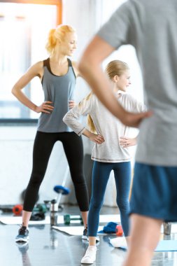 Young woman and cute girl exercising with coach at fitness studio clipart