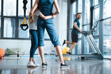 Woman with girl looking at handsome man workout on treadmill at gym clipart