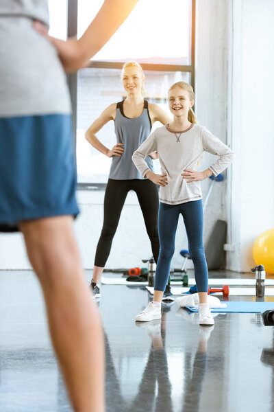 Young woman and cute girl exercising with coach at fitness studio
