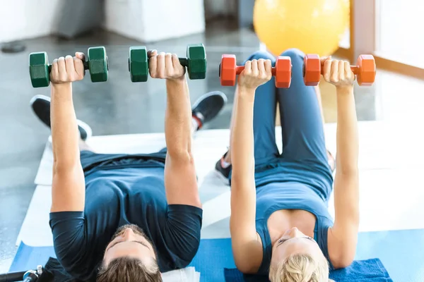 Couple of young fitness people exercising with dumbbells at fitness studio — Stock Photo, Image