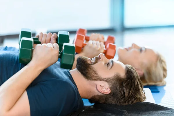 Couple of young fitness people exercising with dumbbells at fitness studio — Stock Photo, Image