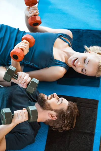Couple of young fitness people exercising with dumbbells at fitness studio — Stock Photo, Image