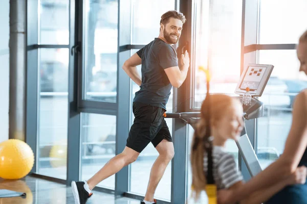 Woman with girl looking at handsome man workout on treadmill at gym — Stock Photo, Image