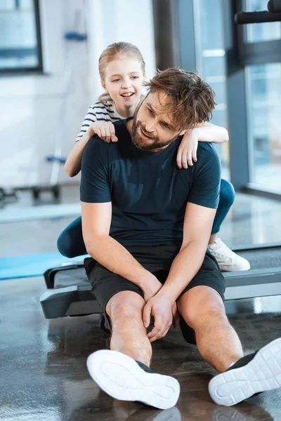 Niña abrazar cansado padre sentado después del entrenamiento en la cinta de correr en el gimnasio —  Fotos de Stock