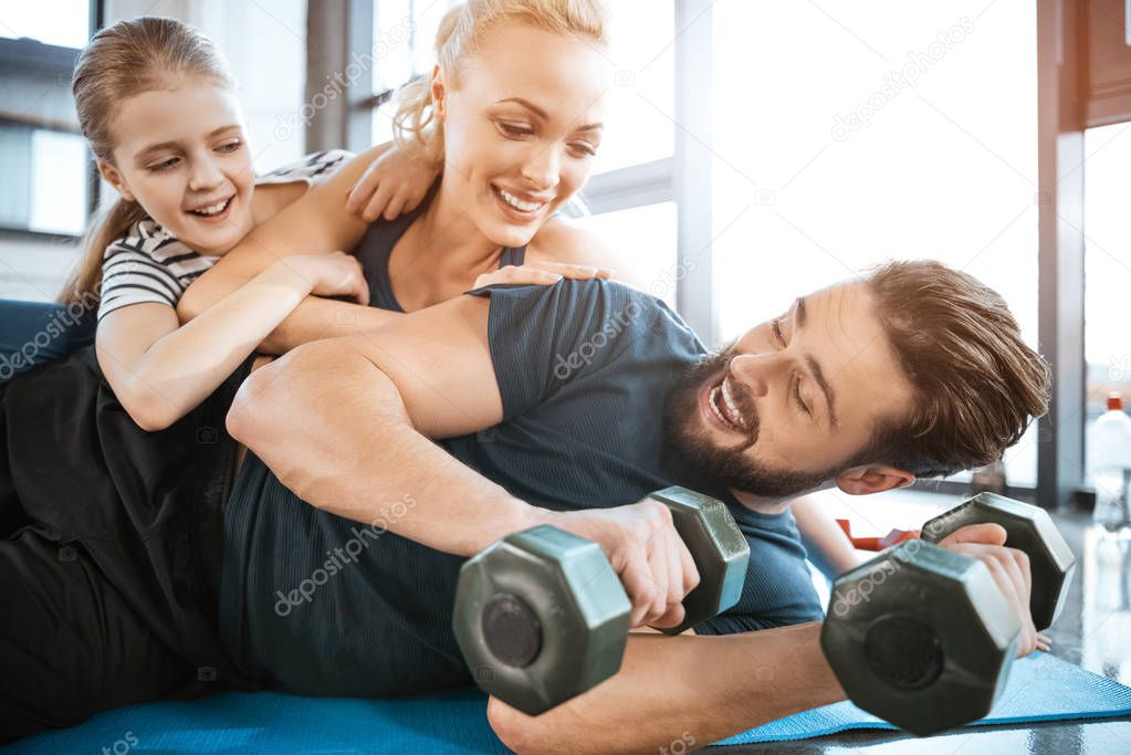 Happy family having fun at gym, man holding dumbbells