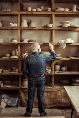 Arkadan görünüş raflar seramik ürünler ile yakın duran ve Atölyesi'nde bir şey ararken üst düzey Potter